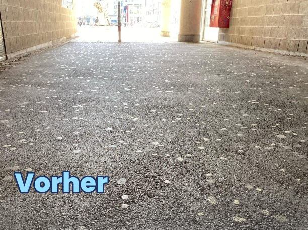 Grauer Bodenbelag mit dicht verteilten eingetretenen Kaugummiresten in einem Durchgang