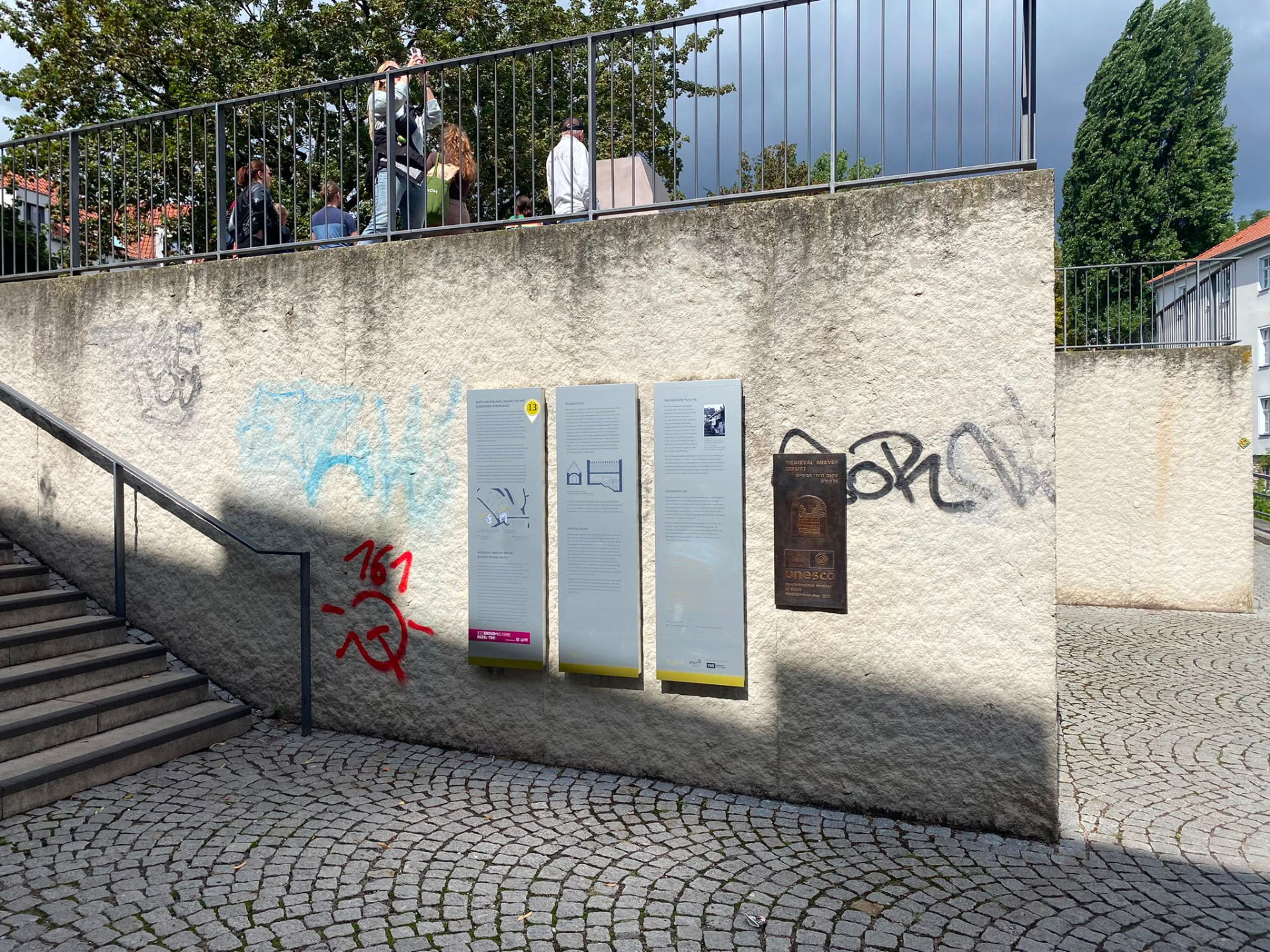 Historische Mauer mit Informationstafeln und Graffiti neben einer Treppe